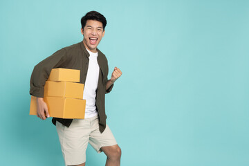 Happy Asian man holding package parcel box and hands up raised arms isolated on green background,...