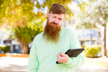 Fototapeta premium red hair young adult man feeling sad and whiney with an unhappy look and crying with a touch screen pad
