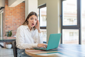 young pretty woman looking happy, astonished and surprised. working with a laptop