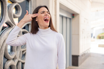 pretty young adult woman looking unhappy and stressed, suicide gesture making gun sign with hand, pointing to head