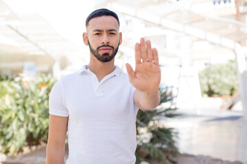 Fototapeta premium young handsome man looking serious, stern, displeased and angry showing open palm making stop gesture