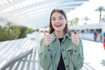 Fototapeta premium young pretty woman smiling joyfully and looking happy, feeling carefree and positive with both thumbs up
