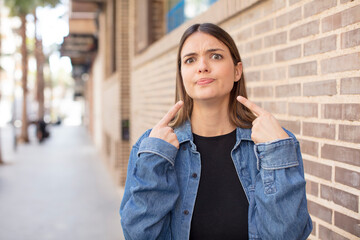 Fototapeta premium young pretty woman with a bad attitude looking proud and aggressive, pointing upwards or making fun sign with hands