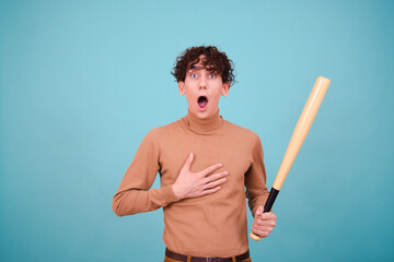 Funny curly student with a baseball bat. Attractive guy posing on a blue background.