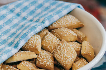 Freshly baked homemade biscuits with sesame covered by towel in bowl.