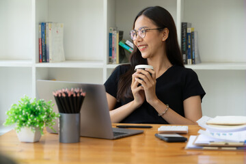 Businesswoman holding a cup of coffee and taking a break from working on her computer.