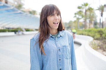 pretty young woman looking happy and friendly, smiling and winking an eye at you with a positive...
