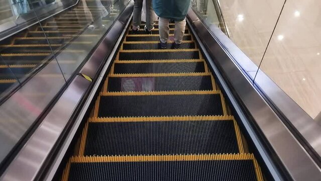 The escalator machine goes down. Go down slowly. In a busy shopping center.