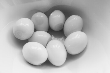 In the kitchen, in a white deep plate, there are several white peeled chicken eggs for preparing a fresh salad, soft focus.