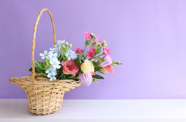 Obraz premium image of delicate pink flowers in the wicker basket over wooden table and purple background