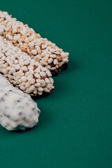 Chocolate bars coated with corn cereals, peanuts pieces and  white icing on green background.