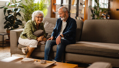 happy senior couple at home sofa having fun laughing together - retirees enjoying free time...