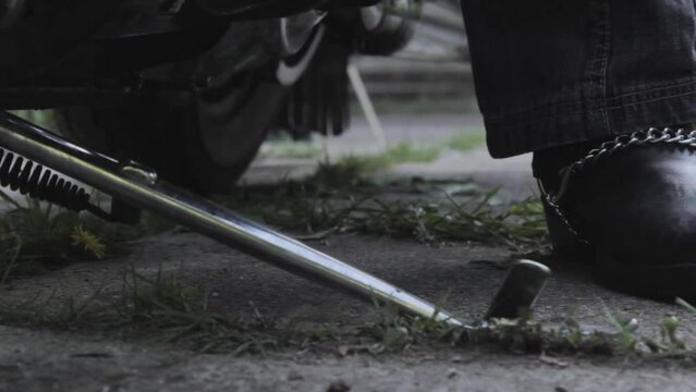 dolly close up shot of motorcyclist dismounting motorcycle and spreading sidestand foot, leather boot with chain
