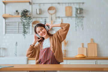 Happy carefree asian woman wearing headphones and ladle singing have fun moving listening to music...