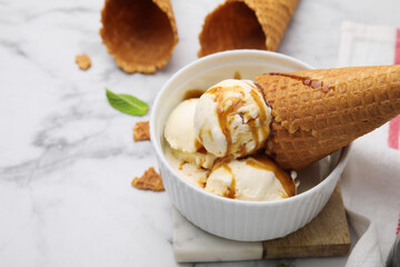 Scoops of ice cream with caramel sauce and cone on white marble table, closeup. Space for text