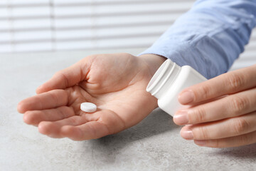 Woman with pill and bottle at light grey table, closeup