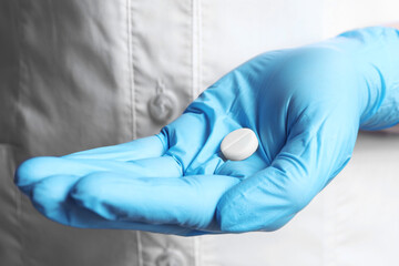 Doctor in medical glove holding pill, closeup view