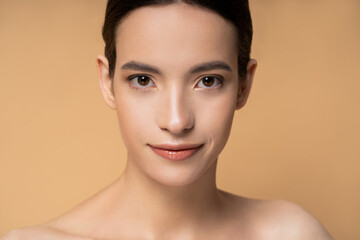 Young asian woman with naked shoulders looking at camera isolated on beige