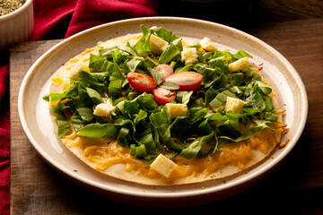 Arugula pizza pan with cheese and cherry tomatoes inside handmade ceramic plate above a wooden table in tow view