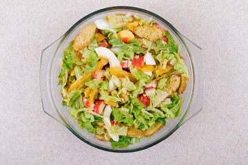 Salad with crab sticks, tomatoes, napa cabbage, eggs, lettuce and croutons in glass bowl. Top view.