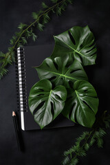 top view of black table top with black notepad with monstera leaves