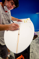 Fototapeta na wymiar Professional surf shaper in action taking measurements in his workshop