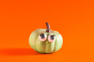 Little green pumpkin with googly eyes on orange background.