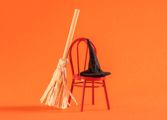 Little red chair with broomstick and witch hat on orange background. Halloween card idea.
