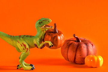 Cute happy dinosaur with pumpkin on orange background.