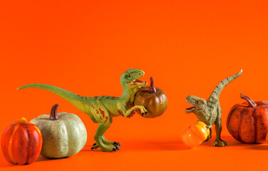 Two cute happy dinosaurs with pumpkins on orange background.