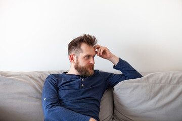Serious bearded man sitting on sofa at home. Handsome man looking away thinking about solving problems. Crisis, depression concept. Selective focus.