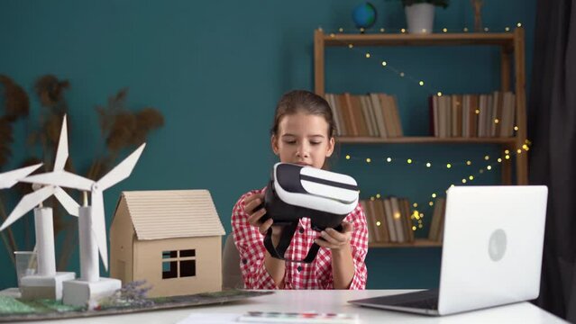 Schoolgirl wearing virtual reality headset works on a wind turbines project, modelling eco-friendly house