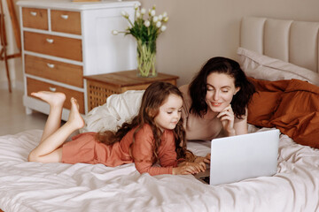 Obraz premium Mother and daughter use laptop on bed on vacation at home. The concept of using online services for online shopping, watching video content or cartoons on streaming services.