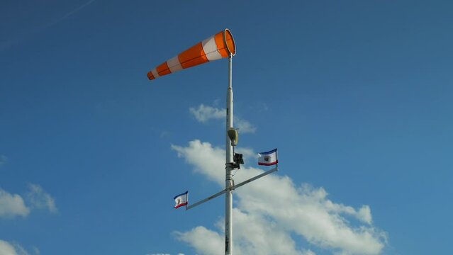 Windscock and flag flutter in the wind on a tall pole. The weather station measures the wind speed and checks the values for the weather forecast