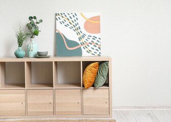 Obraz premium Wooden cabinet with cushions, decor and painting near white wall