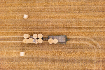 Aerial view of several straw bales on two trailers standing on a dry stubble field