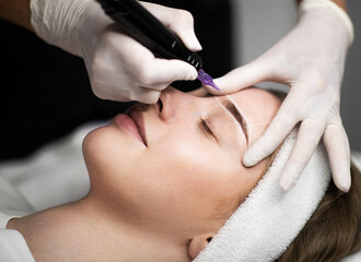 Cosmetologist applying permanent makeup on eyebrows of beautiful young female