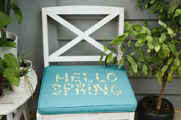 Words HELLO SPRING made out of little flowers near plants outdoors on a seat cushion