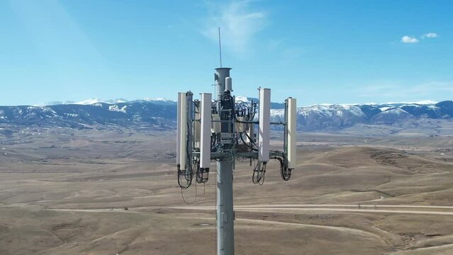 Close-up aerial video of a cell tower in rural landscape on sunny day. Drone shot circling left around the 4G/5G antenna array.