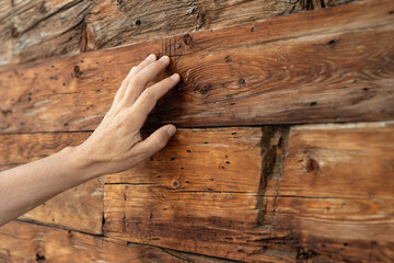 A man's hand lies on the aged wooden wall of a residential building