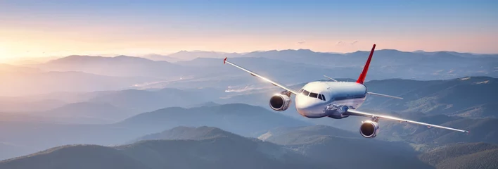 Gordijnen Plane is flying in colorful sky at sunset. Landscape with passenger airplane over mountains ranges and hills in fog, orange sky. Aircraft is landing. Business. Aerial view. Transport. Private Jetlane © den-belitsky