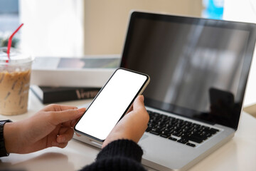 Woman holding mobile phone while working with laptop on white table