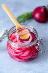 Pickled red onion rings on a wooden spoon on a glass jar. Appetizer, condiment or topping. Healthy fermented food. 