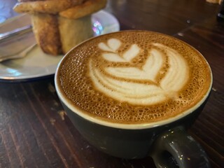 latte coffee with heart pattern art on coffee cup and cinnamon bun on plate