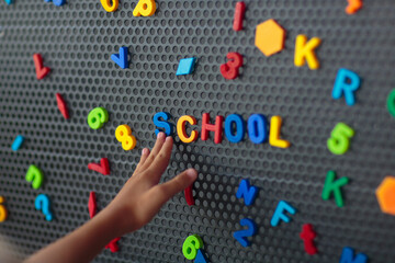 Boy spelling out the word school. Magnet letters.