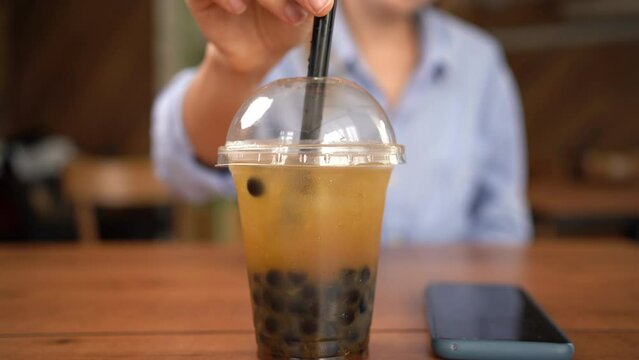 A girl drinking bubble tea in a cafe takes a plastic glass from the table, close-up.