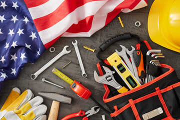 Extend your gratitude to construction workers this Labor Day. Top view shot of american flag, worker equipment, safety helmet, work gloves on concrete grey background