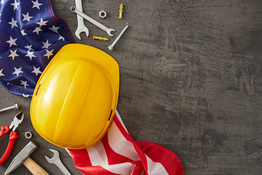 Celebrate the crucial role of construction workers on American Labor Day. Top view shot of american flag, worker equipment, safety helmet on concrete grey background with empty space for promo or text