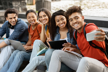 Group of international students taking photo together outdoors on smartphone