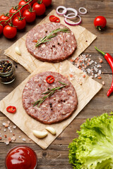 Raw burger patties on parchment and hamburger ingredients on a wooden background.
